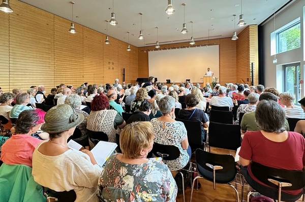 In einem Raum sitzen viele Menschen und hören einem Redner zu