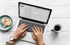 Quelle: Freepik_rawpixel.com Hände bedienen die Tastatur eines Laptops, links stehen Kekse, rechts ein Kaffee