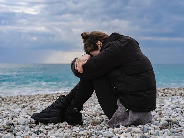 Quelle: Engin Akyurt auf Pixabay Eine Frau sitzt am Strand und hat die Arme und den Kopf auf die Knie gelegt